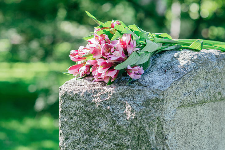 Bunch of pink flowers sitting on stone headstone in cemetery