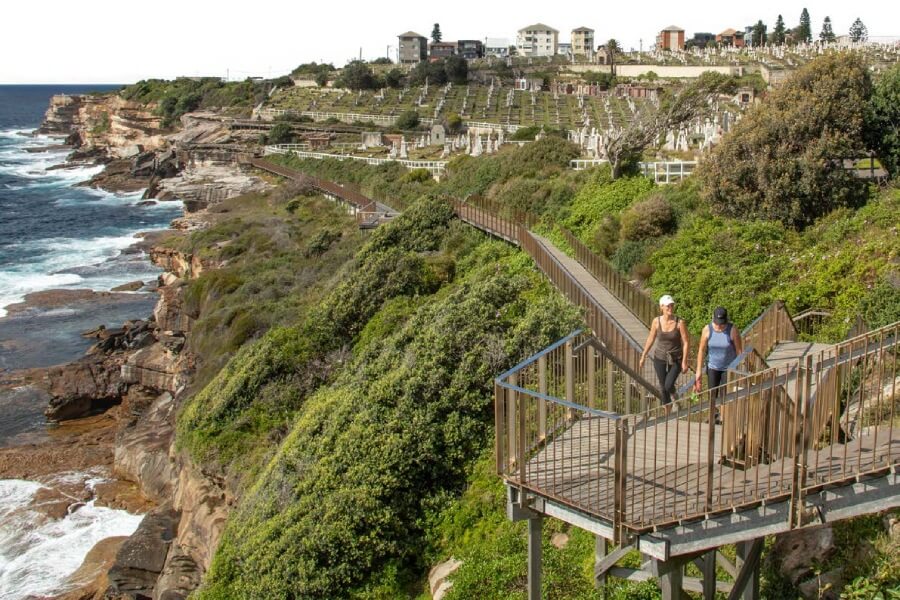 Coastline views with women walking along stairs with cemeteries view in the backrdop.